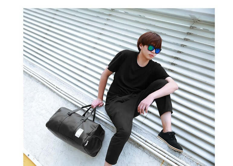 Young man in black outfit holding a waterproof sports fitness bag, showcasing athletic style and functionality.